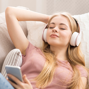 Aufnahme eines weiblichen Teenagers, welche auf der Couch liegt und Kopfhörer trägt